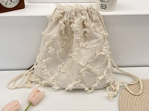 Detailed close-up of beige canvas backpack featuring textured tassel grid pattern and drawstring