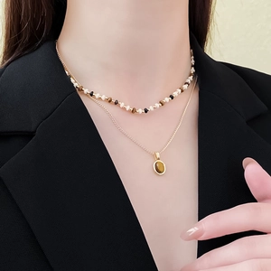 Detailed view of a double-layer necklace featuring brown beads and a gold oval gemstone