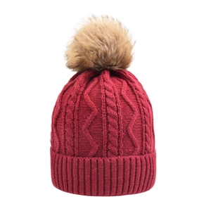 Close-up of wine red cable knit beanie with large faux fur pompom and ribbed cuff