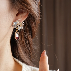 Close-up of floral rhinestone earrings with deep red rectangular crystal pendant