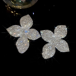 Dettaglio macro di orecchini a lobo a fiore con quattro petali in argento e strass lucidi