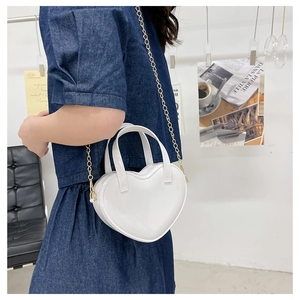 White heart-shaped patent leather crossbody bag with gold chain strap shown on model