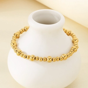 Close-up of polished 18K gold plated stainless steel beaded bracelet on a vase
