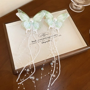 Detailed macro view of butterfly hair clip with green resin wings and pearl tassels