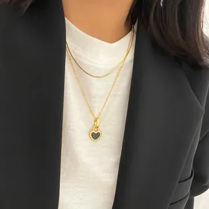 Close-up of double-layer gold snake chain necklace with black heart pendant on a model