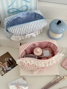 Détail de trousses de maquillage à rayures avec dentelle et nœud sur bureau blanc