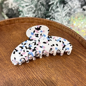 Detail of a large white hair claw clip with colorful floral patterns on a wooden tray