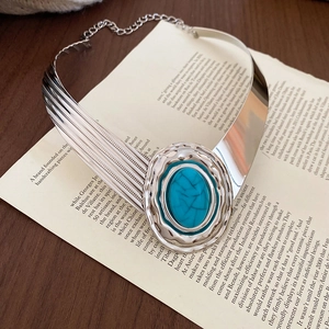 Dettaglio di un girocollo rigido d'argento con un ciondolo ovale in turchese su un libro