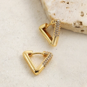 Detail of 18K gold triangular heart earrings with zircon inlay on a textured beige background