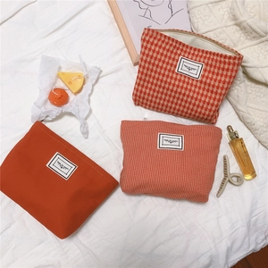 Three-piece set of orange houndstooth and solid canvas cosmetic bags on a cozy white fabric