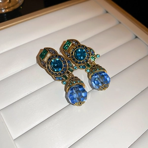 Close-up of vintage gold clip-on earrings featuring blue and green crystal rhinestones