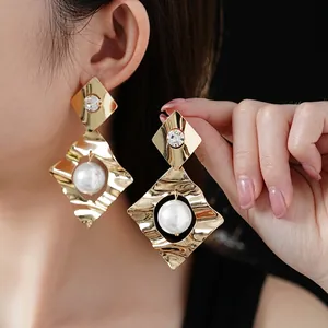Luxury gold rhombus earrings with large pearl and sparkling diamond on dark background