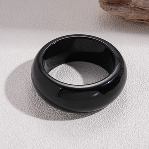 Close-up of polished black resin geometric bangle on a minimalist stone background