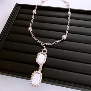 Close-up of a silver glasses-shaped pendant with cubic zirconia on a black tray