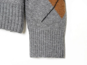 Dettaglio maglione grigio con polsini a costine e motivo a rombi in stile argyle