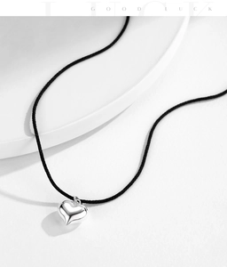 Macro detail of a 925 sterling silver heart pendant on a minimalist black woven cord