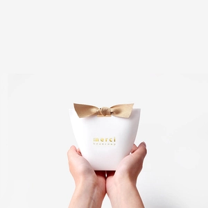 White embossed paper gift box featuring a gold bow and Merci Beaucoup gold foil stamping
