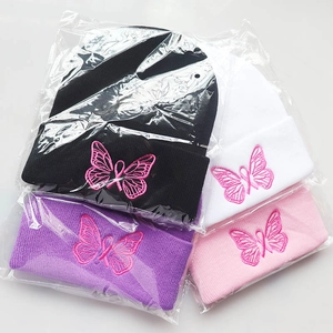 Detailed close-up of pink butterfly embroidery and ribbon on folded knit beanies