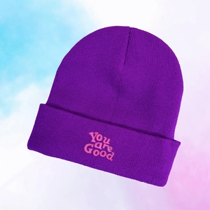 Close-up of You are Good pink embroidery on a purple knitted beanie cuff with fine texture