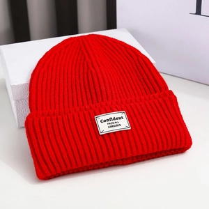 Close-up of red knit beanie featuring a white woven patch with black English text
