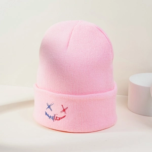 Détail du bonnet en tricot rose avec un smiley brodé bicolore et des yeux en X