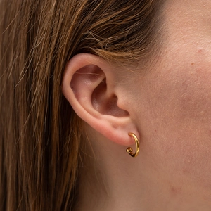 Close-up of a minimalist golden ball hoop earring worn on a female earlobe