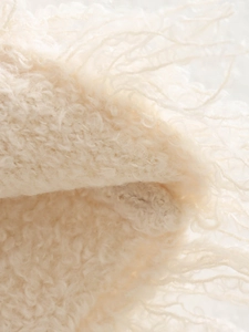 Close-up of beige plush knit fabric texture with decorative fringe detail and soft finish