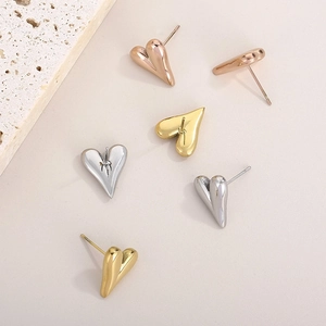 Three heart-shaped stud earrings in gold, silver, and rose gold on a textured stone