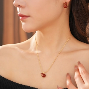 Close-up of a gold 18k plated gourd necklace and earrings set with red enamel detail