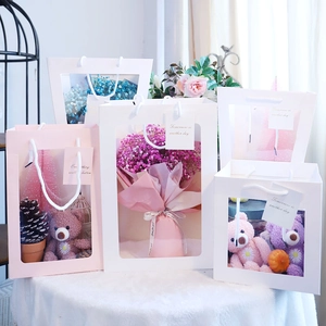 Detail of transparent gift bags with plush bears and flowers on a soft white surface