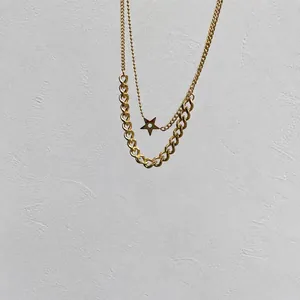 Detail of gold double-layer necklace featuring star pendant and thick Cuban link chain