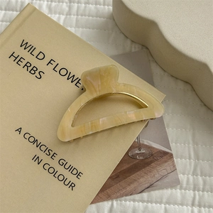 Detail of a minimalist beige marble acetate hair claw clip placed on a book