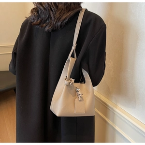 Detail of beige lychee textured leather bucket bag with tie-strap and lock on a model