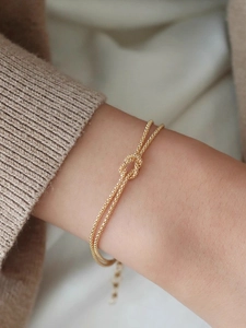 Detailed close-up of a gold-plated knot bracelet on a wrist featuring a textured chain