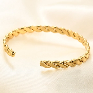 Polished gold C-shape twisted open cuff bracelet on elegant cream silk background