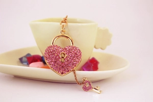 Detail of a pink crystal encrusted heart lock and key keychain on a coffee cup