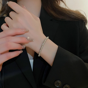 Close-up of a silver zircon bracelet worn by a model against a black blazer background