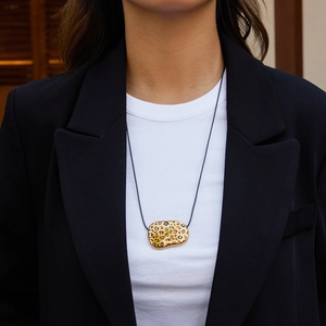 Close-up of leopard print metal pendant with black cord on model wearing a black blazer