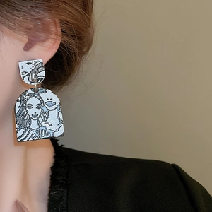 Close-up of abstract face art earrings featuring minimalist black lines on white acrylic