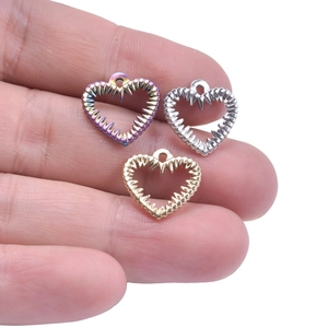 Three tiny serrated heart pendants in gold, silver, and rainbow on a palm for size comparison