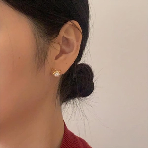 Close-up of golden bow-shaped pearl stud earring worn on the earlobe with elegant detail