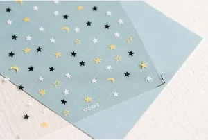 Close-up of KX040-2 nail stickers with yellow moon and gold star patterns on blue mat