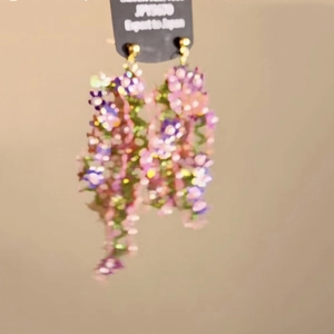 Detail of floral tassel earrings in pink and purple tones hanging on a black card