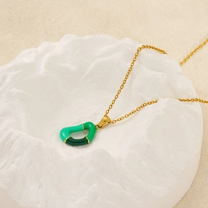 Gold stainless steel necklace with green enamel abstract pendant on artistic display