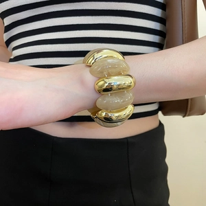 Close-up of gold metal and amber acrylic oval link bracelet worn on a female wrist
