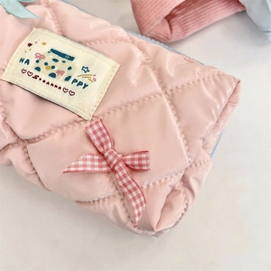 Detailed macro view of pink quilted glossy fabric with bow and Happy label on pouch