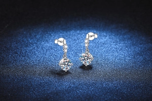 Macro detail of dangling silver earrings with three small diamonds and a large moissanite