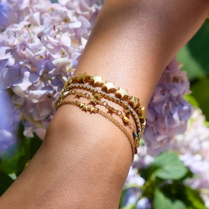 Close-up of gold star charms and zircon layered bracelets worn against purple flowers