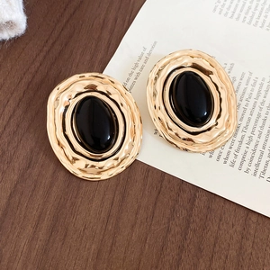 Dettaglio di orecchini vintage dorati con pietra nera ovale e finitura martellata