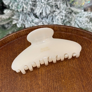 Detail of a creamy white acetate hair claw clip with gold lettering on a wooden base